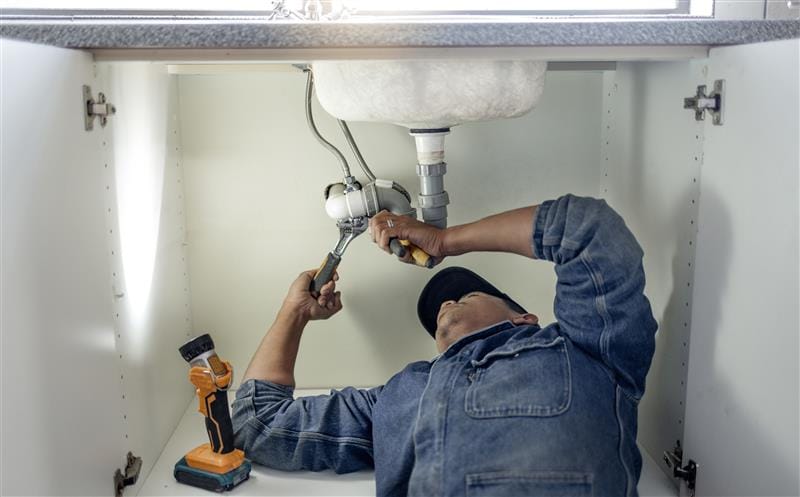 Plumber repairing pipes beneath a bathroom sink in Marina