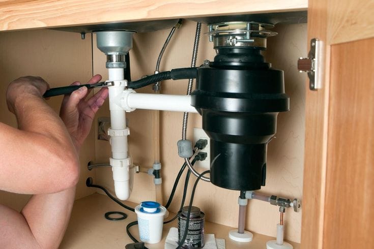 Plumber installing a garbage disposal beneath a kitchen sink in Marina