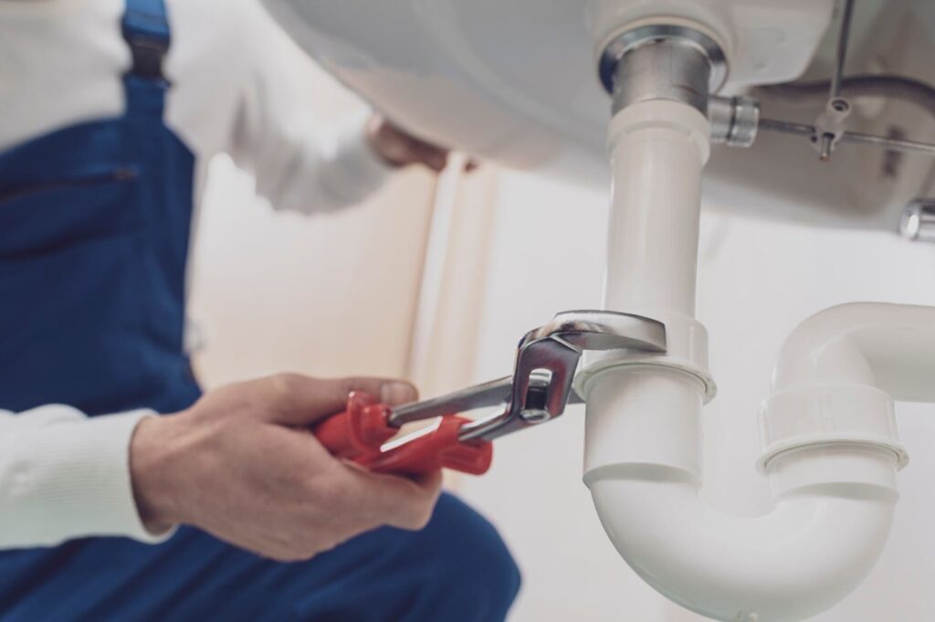 Plumber repairing a white drain pipe beneath a sink in Marina