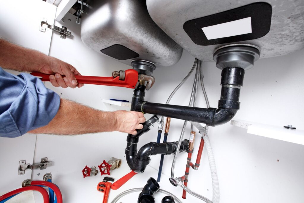 Plumber repairing drain pipes beneath a kitchen sink in Marina